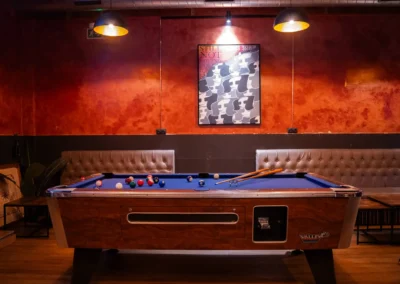 Valley brand professional pool table surrounded by tufted leather booths and abstract face artwork in a dimly lit cannabis club.