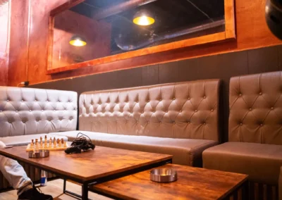 Corner booth seating with tufted leather benches, a large wall mirror, and wooden tables holding a chess set and video game controllers.