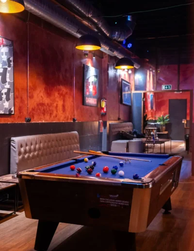 Angled view of a pool table, leather seating, and a 'Darkness' poster under exposed ceiling ductwork in a cannabis lounge.