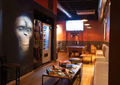 Main lounge area featuring a large, illuminated 3D monkey face wall sculpture, board games on a table, and a pool table in the background.