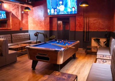 Pool table and extensive leather seating area in a warmly lit cannabis social club with a television screen.